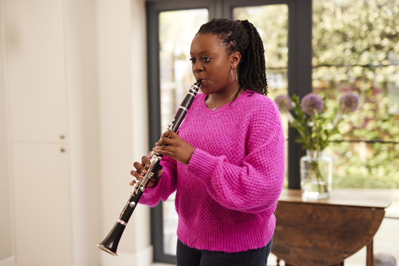 A young woman in a pink jumper plays the clarinet