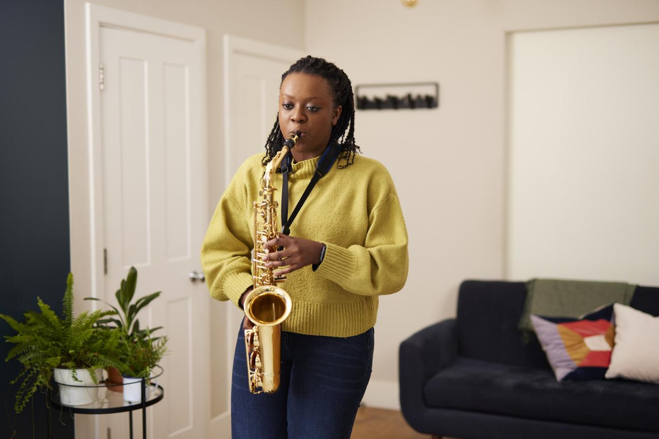 A young woman in a yellow jumper plays the saxophone
